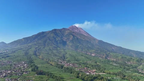 Drone shot of an active volcano releasing smoke with villages and farmland in Stock Footage 316301906