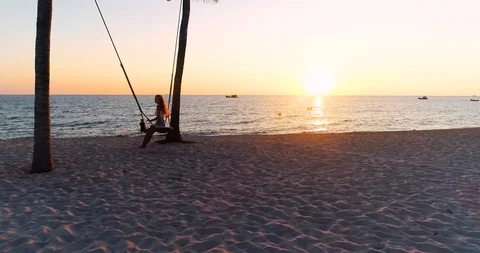 Drone shot aerial view of young women swinging at tropical sandy beach Stock Footage 113131296