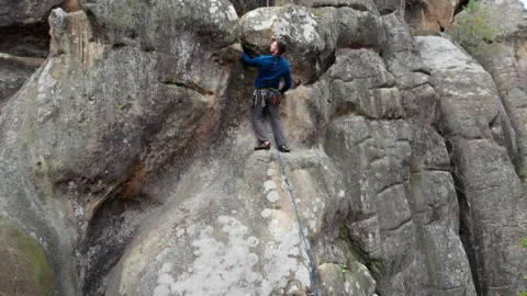 Drone shot of athlete moving up rugged cliff with chalked holds and protective Stock Footage 346551001