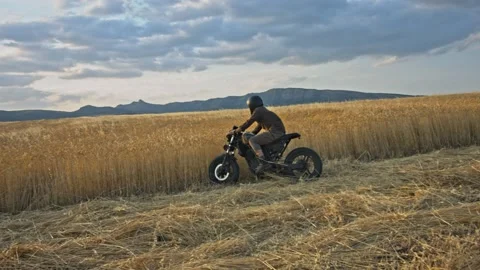 Drone shot of a bearded man riding an old cafe racer motorcycle in wheat field Stock Footage 140362011