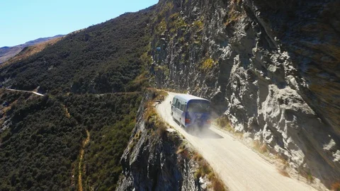 Drone shot of blue van driving down thin dusty mountain road in New Zealand Stock Footage 90267593