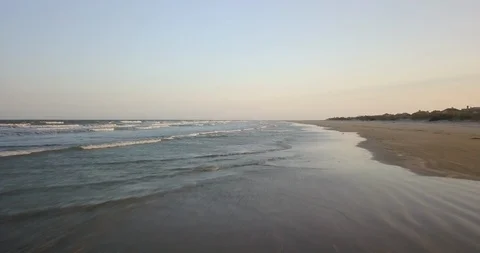Drone shot of calm waves flow towards empty sandy shore in the late afternoon Stock Footage 126610328