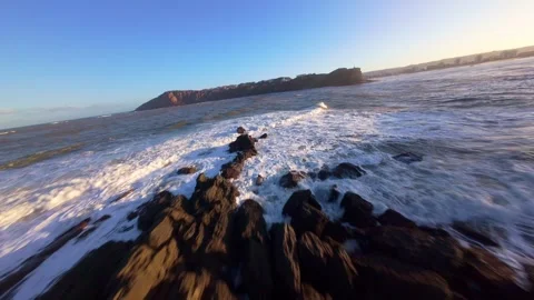 Drone shot captures dramatic ocean surf and rocky shore at golden hour Stock Footage 344581266