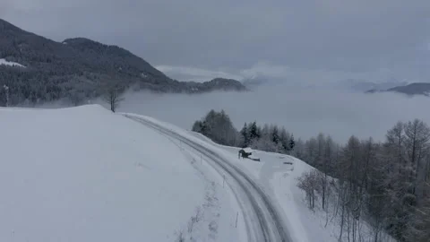 Drone shot of a car coming into the frame on a snowy road in the middle of t Stock Footage 145699926