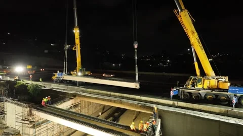 Drone shot of a concrete beam being lifted to build a bridge at night Video stock 342221124