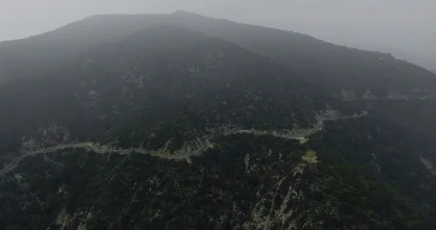 Drone shot dark mountains with a forest and a winding road under a foggy shroud Video stock 119075419