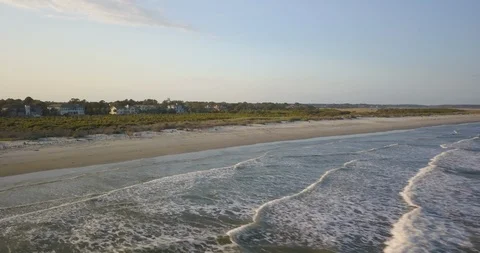 Drone shot of empty waves at the shore of a sandy beach with houses in the back Video stock 126609919