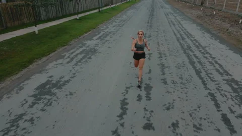 Drone shot of female runner passing steadily along road lined with fence Stock Footage 339622997