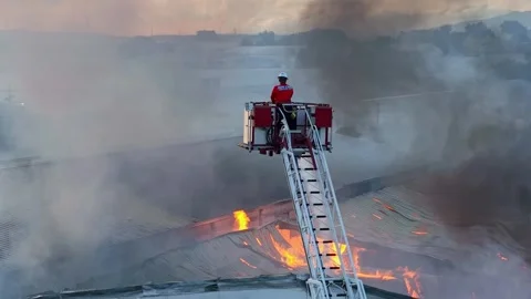 Drone shot of firefighter on ladder spraying water on burning building Stock Footage 282505784