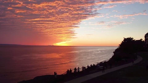 Drone shot of firey sunset over ocean with people watching from cliff. 스톡 동영상 77732285