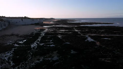 Drone shot flying backwards over rocks at low tide next to the cliffs at sunset. Stock Footage 146743978