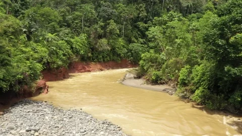 Drone shot that is flying over a large brown fast flowing tropical stream Stock Footage 142757606