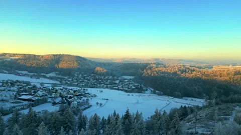 Drone shot flying up over winter trees revealing golden sunset and small village Stock Footage 231223659
