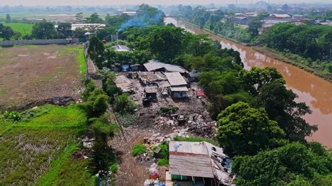 Drone shot of illegal waste dumping site located between muddy river and Stock Footage 333551284