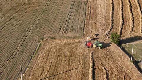 Drone shot of John Deere tractor baling hay in Alseno field with curved rows Stock Footage 310596476