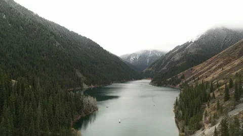 Drone shot lake surrounded by forest with mountain views in cloudy weather Stock Footage 227125768