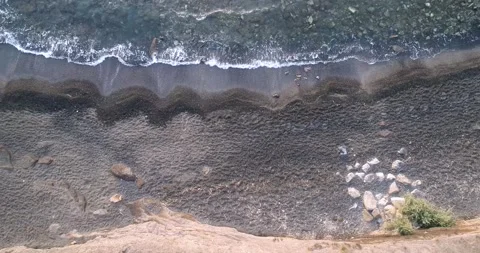 Drone shot looking down at waves coming on the black sand beach in Cap d'Agde FR Stock Footage 186470757