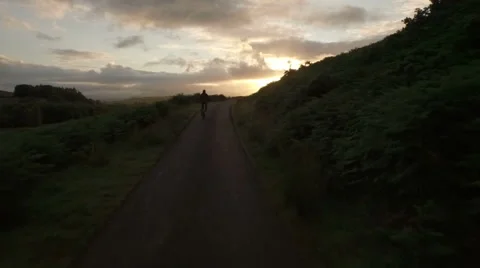 Drone shot of a man cyling along a quiet road in Scotland during sunrise Stock Footage 62111554