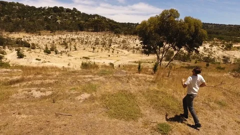 Drone shot of man running to cliff face scared and looking around in the desert Stock Footage 122472173
