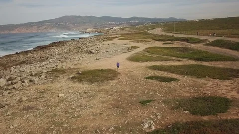 Drone shot of a man running on the ground along the seacoast in Cascais Video stock 114854612