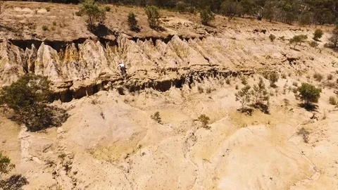 Drone shot of man running scared climbing a cliff of sand rock in desert Stock Footage 122440607