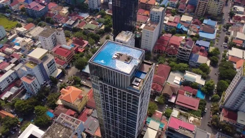 Drone shot of a modern high-rise with a rooftop pool rising above dense city Stock Footage 323426053