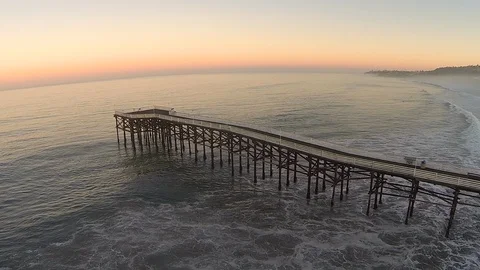 Drone shot of ocean beach waves crashing beneath a long wooden fishing pier. Stock Footage 129061659