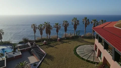 Drone shot of the ocean coast with waves, palms and mountains in the golden hour Stock Footage 289823360