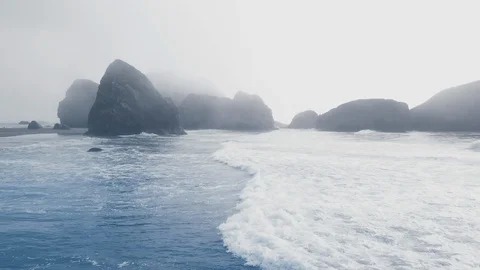 Drone shot of ocean waves and protruding cliffs in the fog Ariya's Beach Video stock 123392157