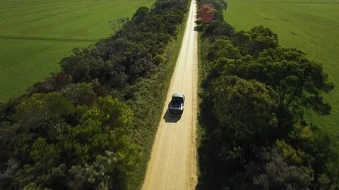 Drone shot of old 1950s car driving down country road into the sun. Stock Footage 87830360
