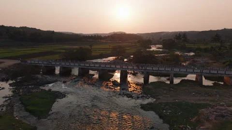 Drone shot over a bridge and a river flowing next to fields in rural India Stock Footage 305259609