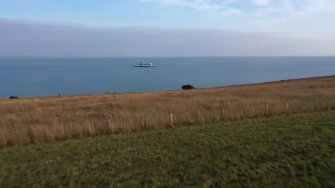 Drone shot over fields and a cliff edge revealing the ocean and a ferry. 4k Stock Footage 147369438