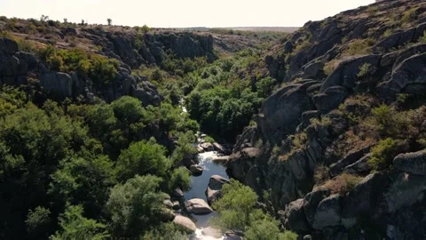 Drone shot over a narrow rocky canyon with trees and a small river Video stock 201635181