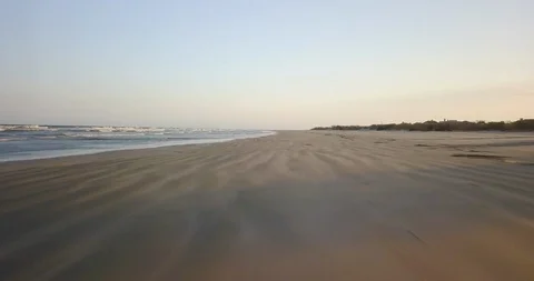 Drone shot passing through empty sandy beach in the late afternoon, calm waves Video stock 126610255