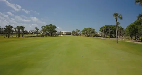 Drone shot passing through green golf course with trees and path on sunny day Stock Footage 126609411