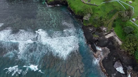 Drone shot of powerful Pacific waves crashing against the rugged volcanic Stock Footage 325942322