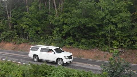 Drone Shot Profile of White SUV driving on a Road through the Rocky Mountains Stock Footage