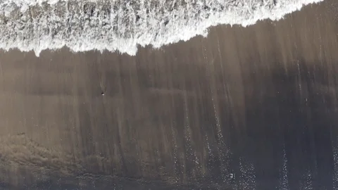 Drone shot pull back of peaceful waves roll into a black sand beach shore Stock Footage 103222864