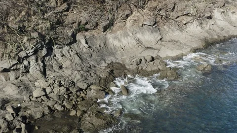 Drone shot pulling back from rocky shoreline as wave splash 스톡 동영상 103220867