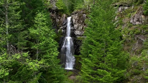 Drone shot pushing in past trees towards big waterfall cascading down through a Видео 345051883