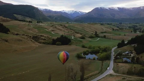Drone shot of rainbow colored hot air balloon rising above lake and mountains Stock Footage 90266833