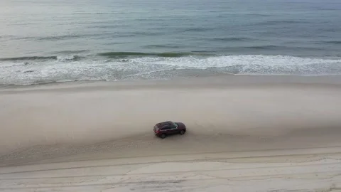 Drone Shot of a Red SUV Driving Along a Sandy Ocean Beach Stock Footage 324549743