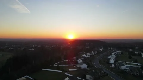 Drone shot rising and moving towards a sunset over a quiet suburban town and Stock Footage 228699695