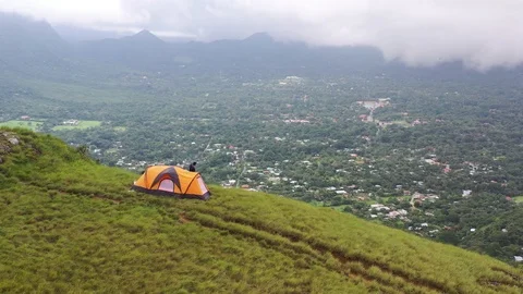 Drone shot rotating around camp tent on top of mountain overlooking town green Stock Footage 114815867