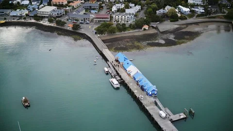Drone shot small jetty with blue and white buildings beside coast Stock Footage 90316633