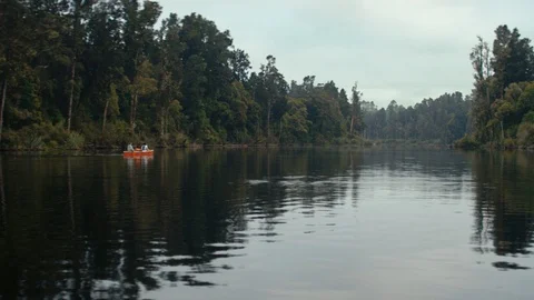 Drone shot small orange boat on still river surrounded by trees in New Zealand Stock Footage 89998717