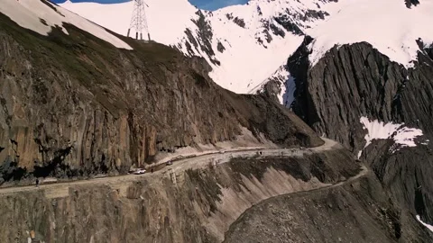 Drone shot of snow-draped cliffs and vehicles carving through Zojila Pass. Stock Footage 310806694