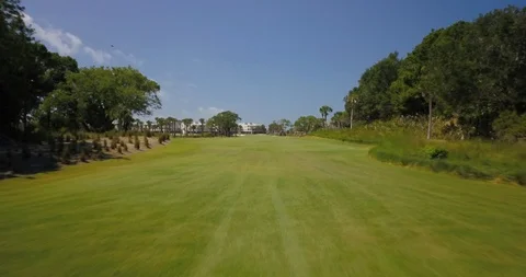 Drone shot through green grass golf course with path and golf resort in the back Stock Footage 126609242