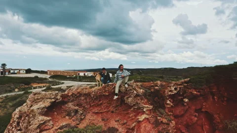 Drone shot of two men sitting on top of cliff with a dog Stock Footage 203595024