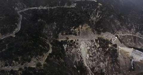 Drone shot two winding roads, a dam and a reservoir in wooded mountains Video stock 119076210